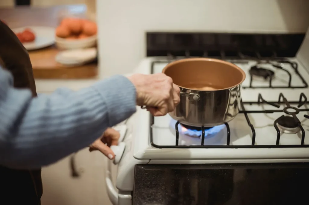 Iemand zet een pan op een brandende gaspit van een wit gasfornuis