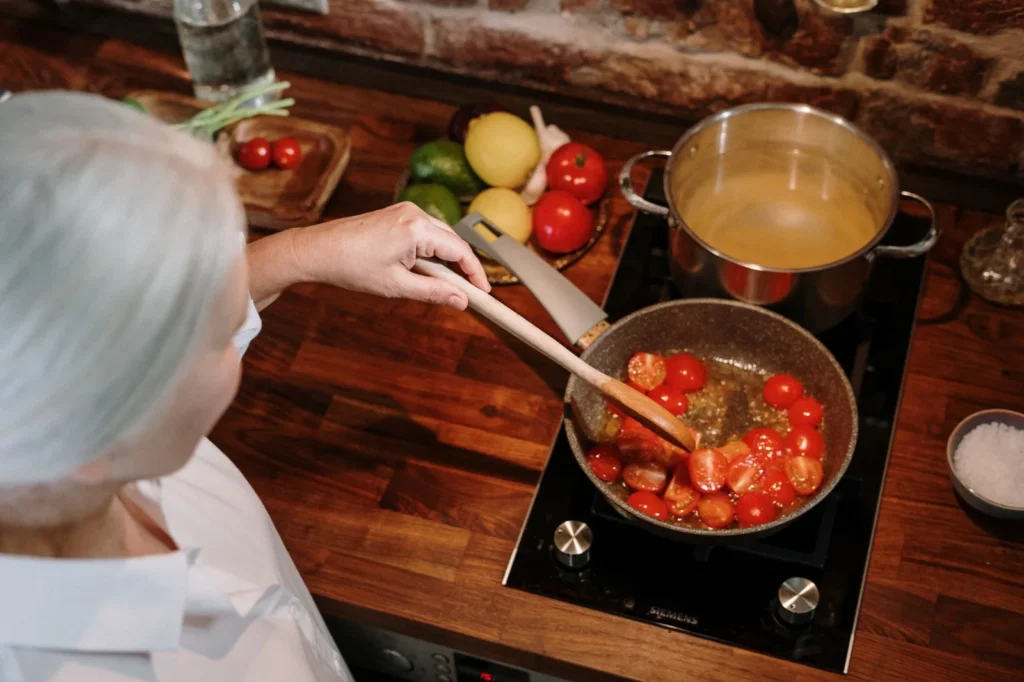 Oudere vrouw roert tomatensaus in een pan op een elektrische kookplaat