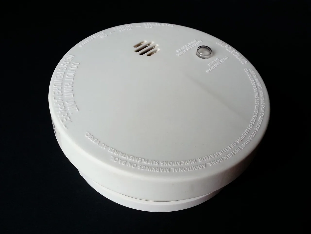 Close-up van een witte rookmelder met de ronde testknop en het controlelampje bovenop