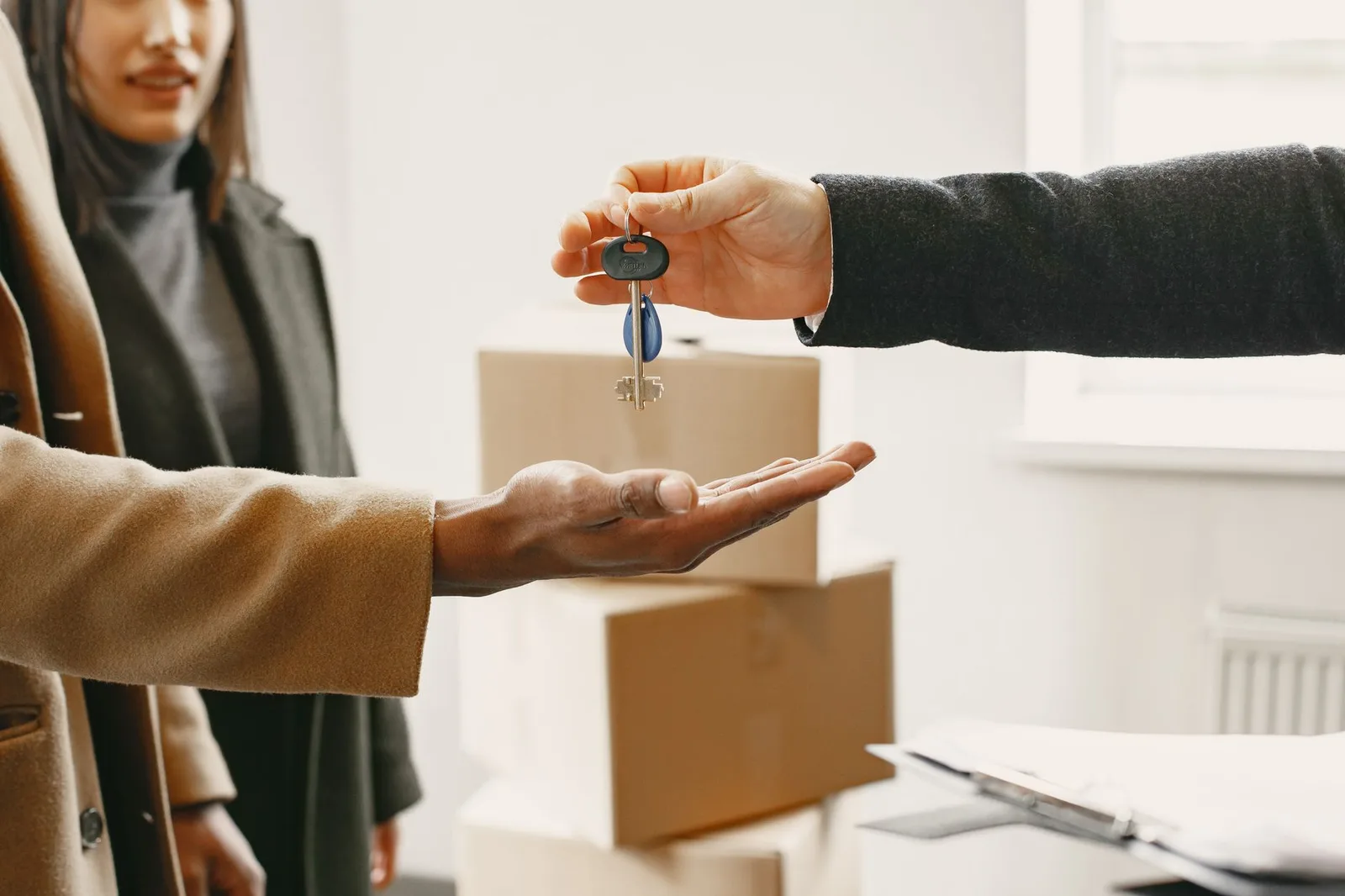 Sleuteloverdracht bij een nieuw huis: een hand geeft een sleutelbos aan de nieuwe bewoner, met verhuisdozen op de achtergrond