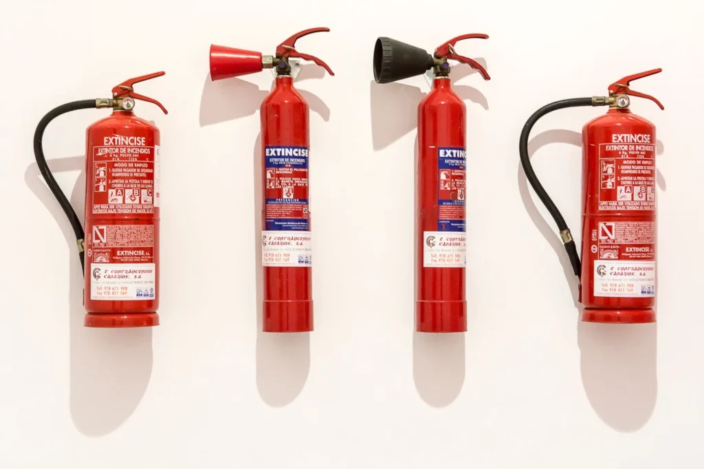 Vier brandblussers naast elkaar aan een witte muur: twee poederblussers met slang en twee CO2-blussers met een trechtervormige hoorn