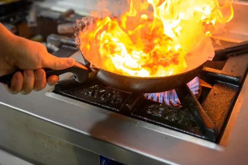 Hoge vlammen slaan uit een koekenpan op een brandende gaspit