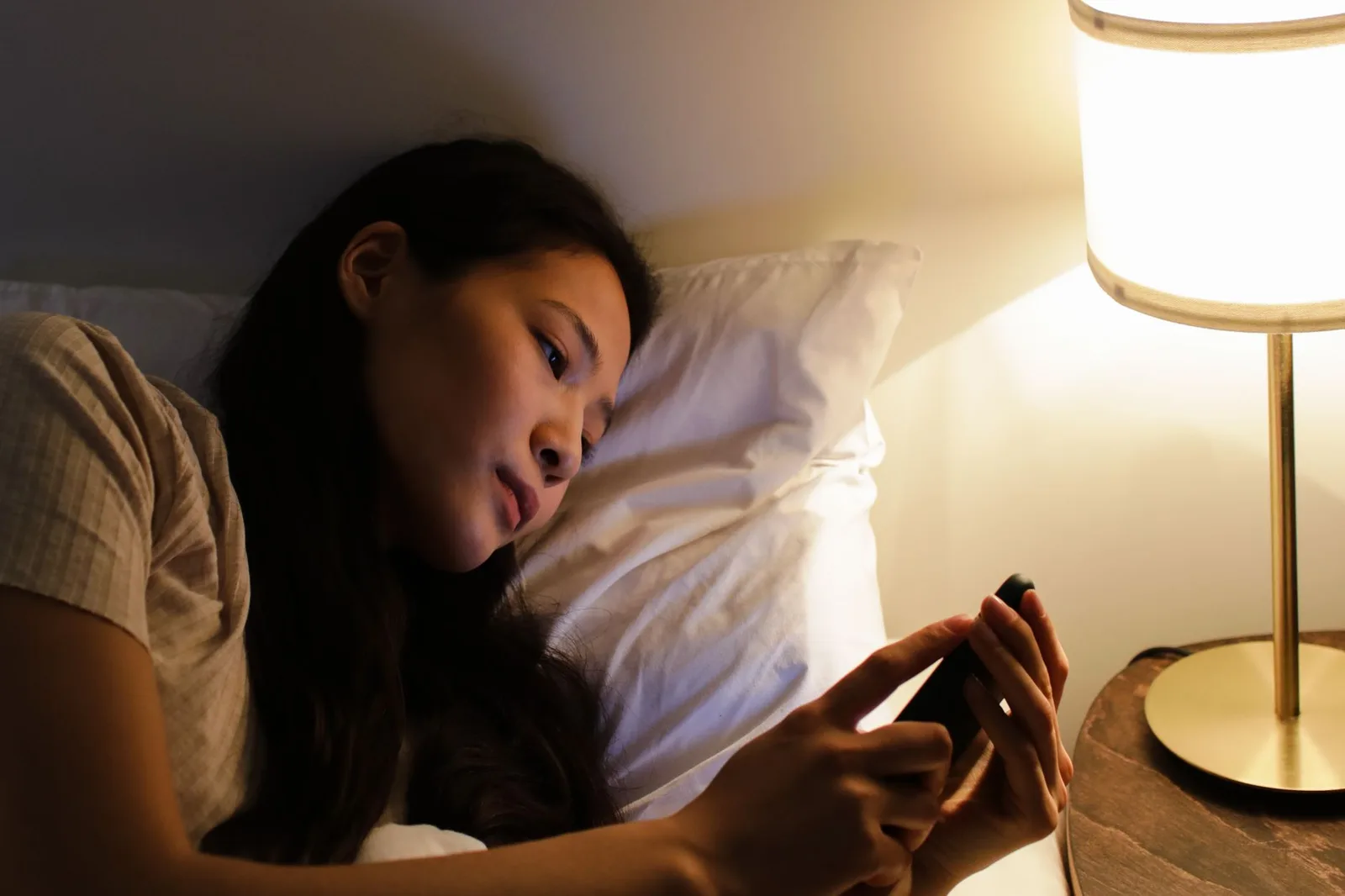 Vrouw ligt 's avonds in bed bij het licht van een nachtlamp en kijkt op haar smartphone, zoals wanneer 's nachts een alarmmelding binnenkomt